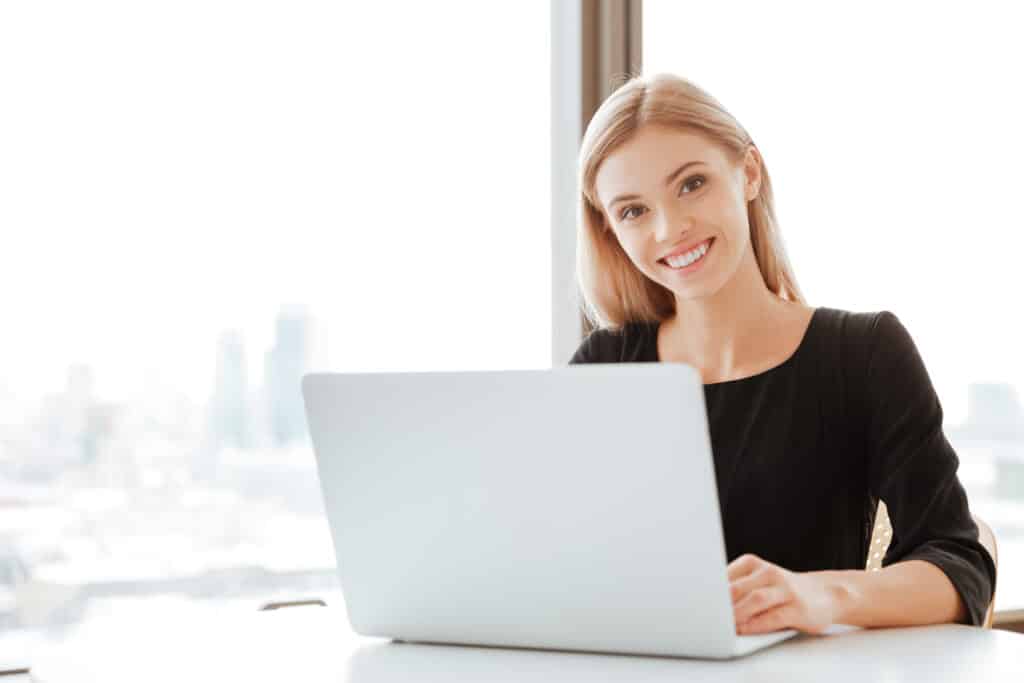 Graphicstock picture of cheerful young lady worker sitting in office while using laptop computer and typing by keyboard look at camera rog pwjlhx