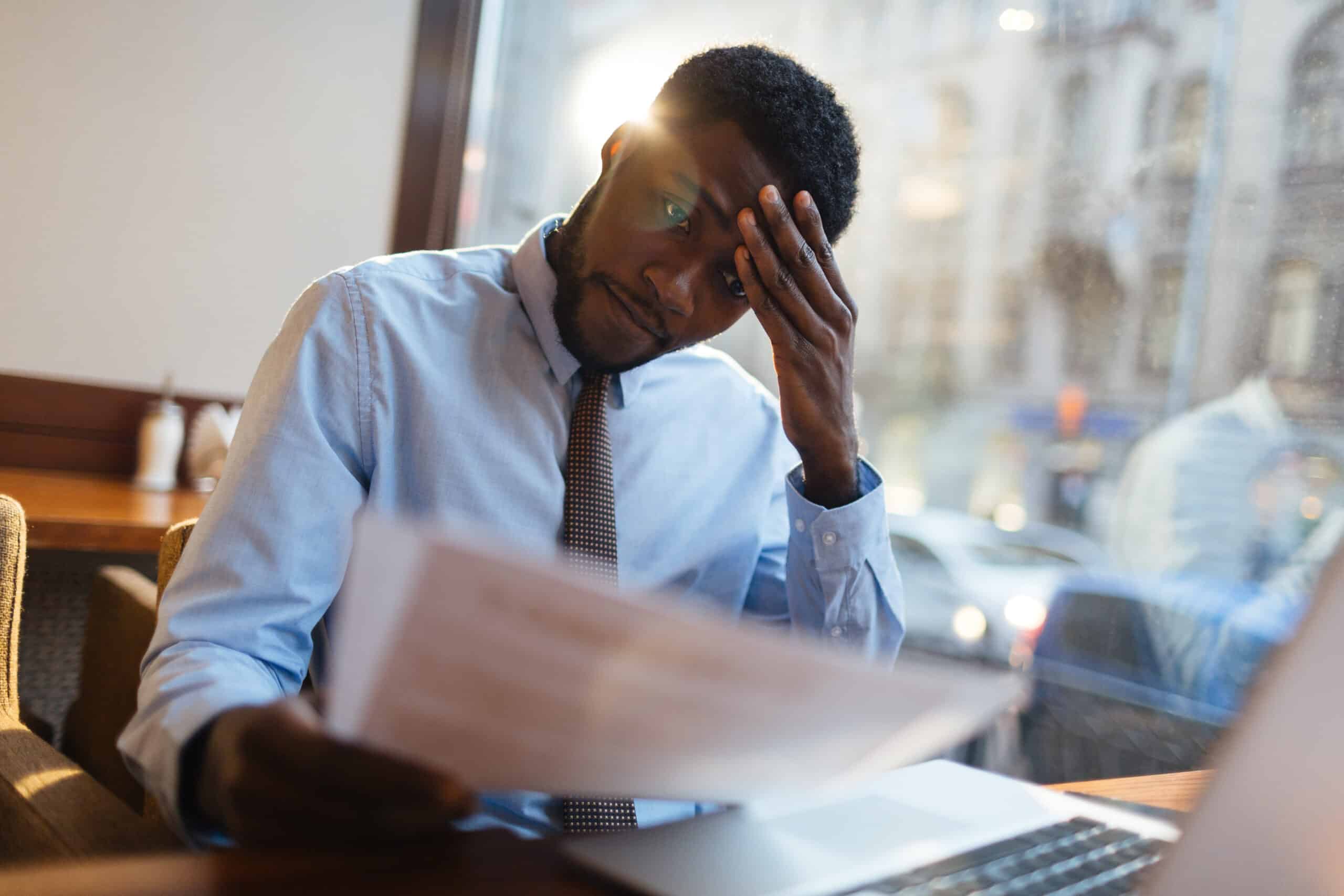 Top 10 Mistakes Every New Entrepreneur Should Avoid 3 Storyblocks focused african american office manager sitting at cafe table with laptop reading important documents with puzzled expression and holding head with his hand rnev5oh1kg scaled